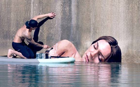 Художник рисува върху стени, качен на сърфа си